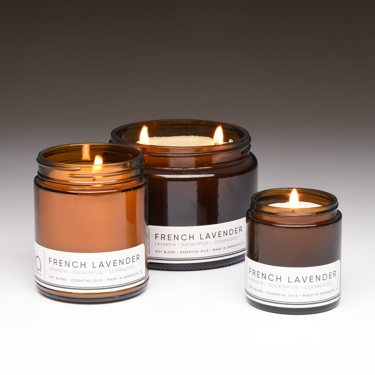 Three amber soy candle jars in different sizes, each with a lit wick