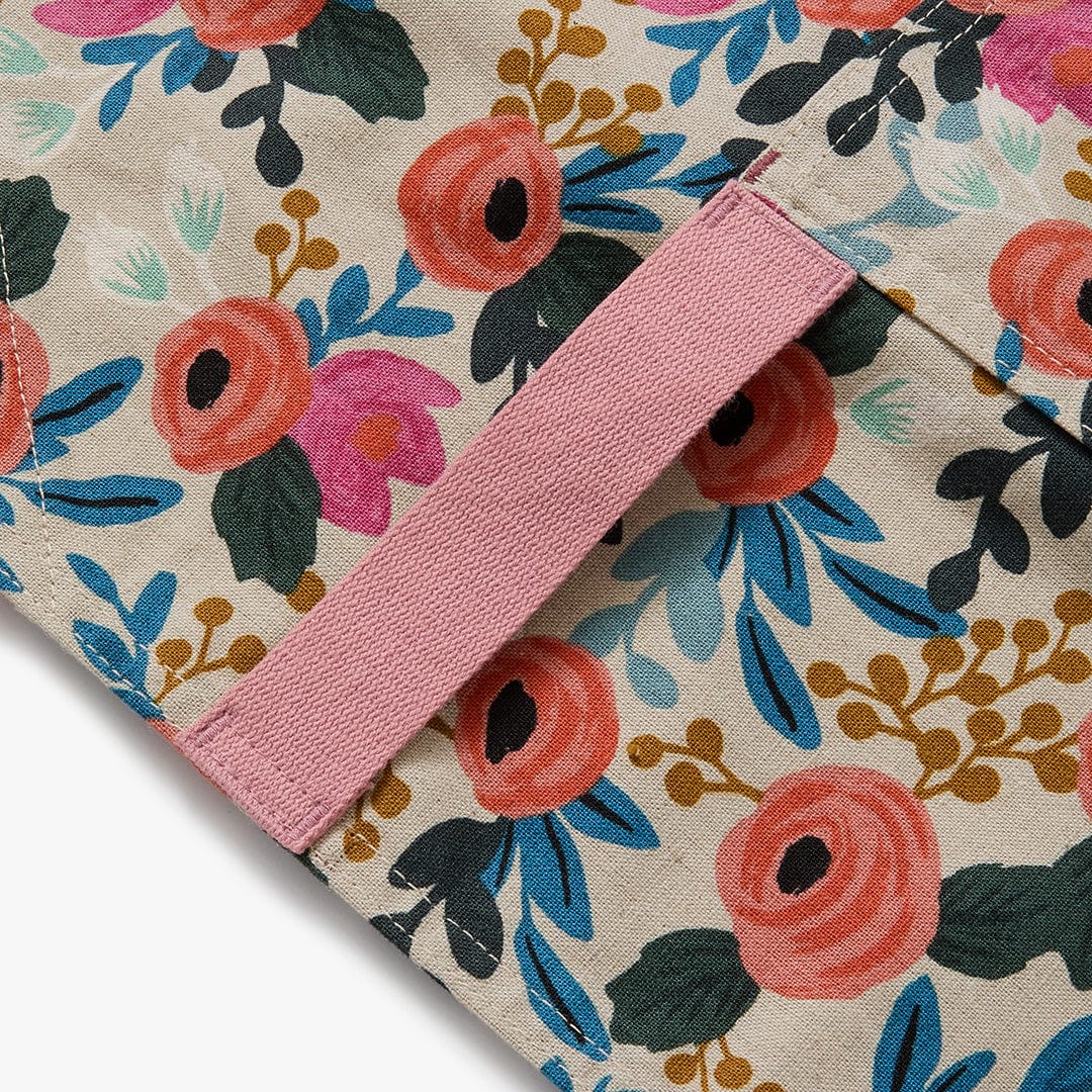 Floral crossback apron strap detail with pink webbing across natural background.