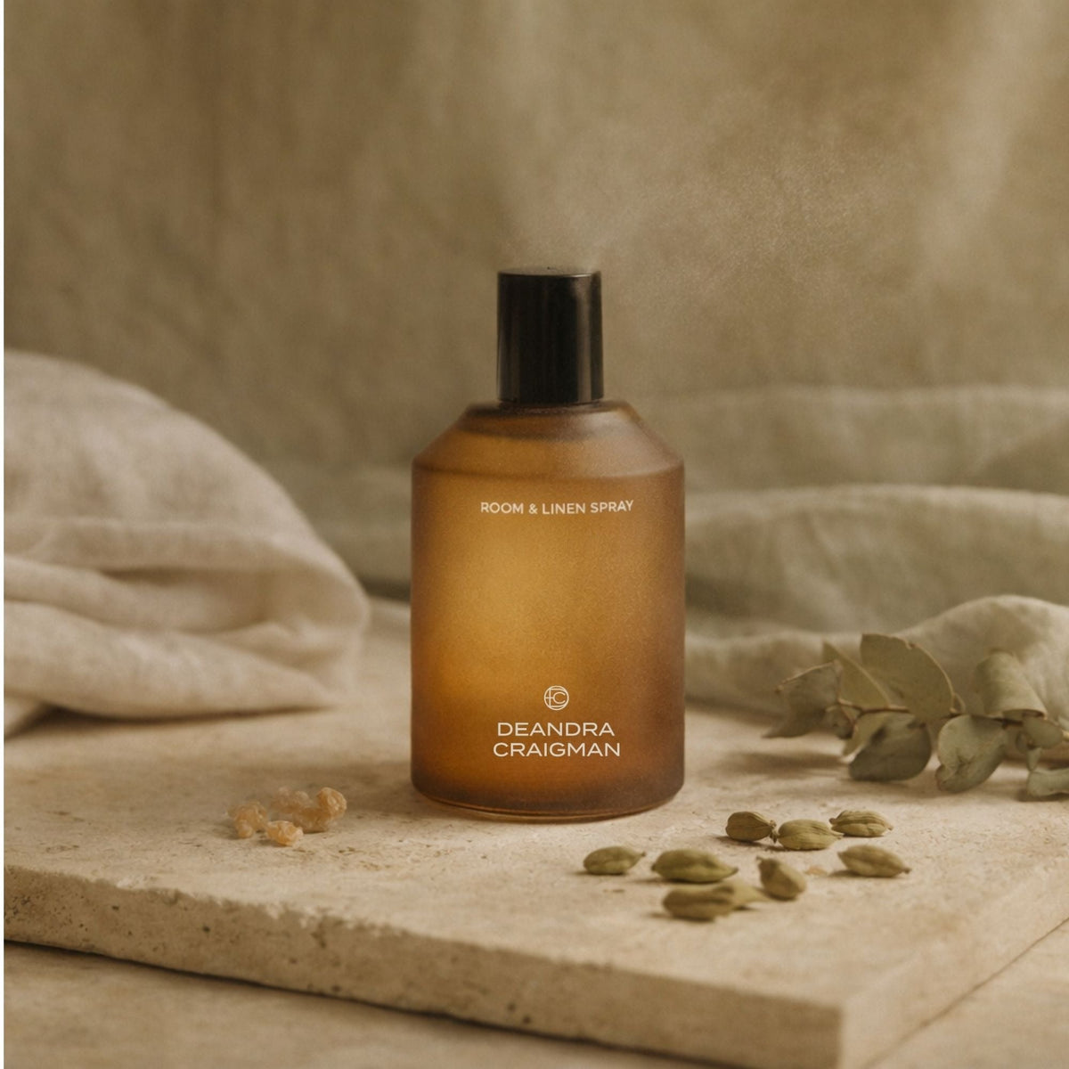 Amber room and linen spray bottle with black cap on folded linen