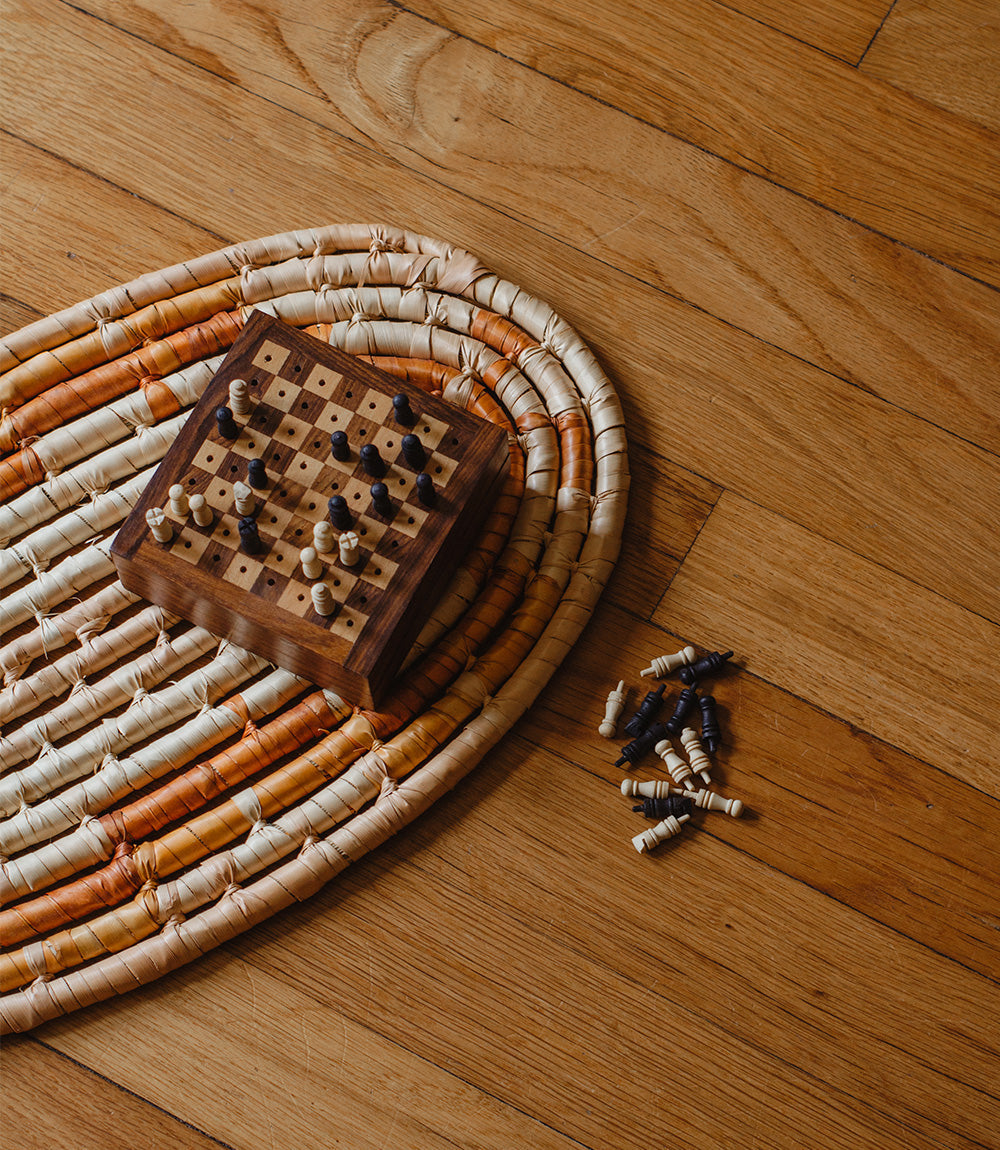 Wooden chessboard with black and light pieces on a woven circular travel mat