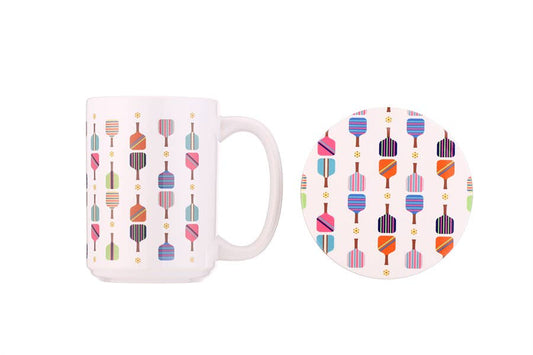 White mug and round coaster printed with colorful pickleball paddles and balls.