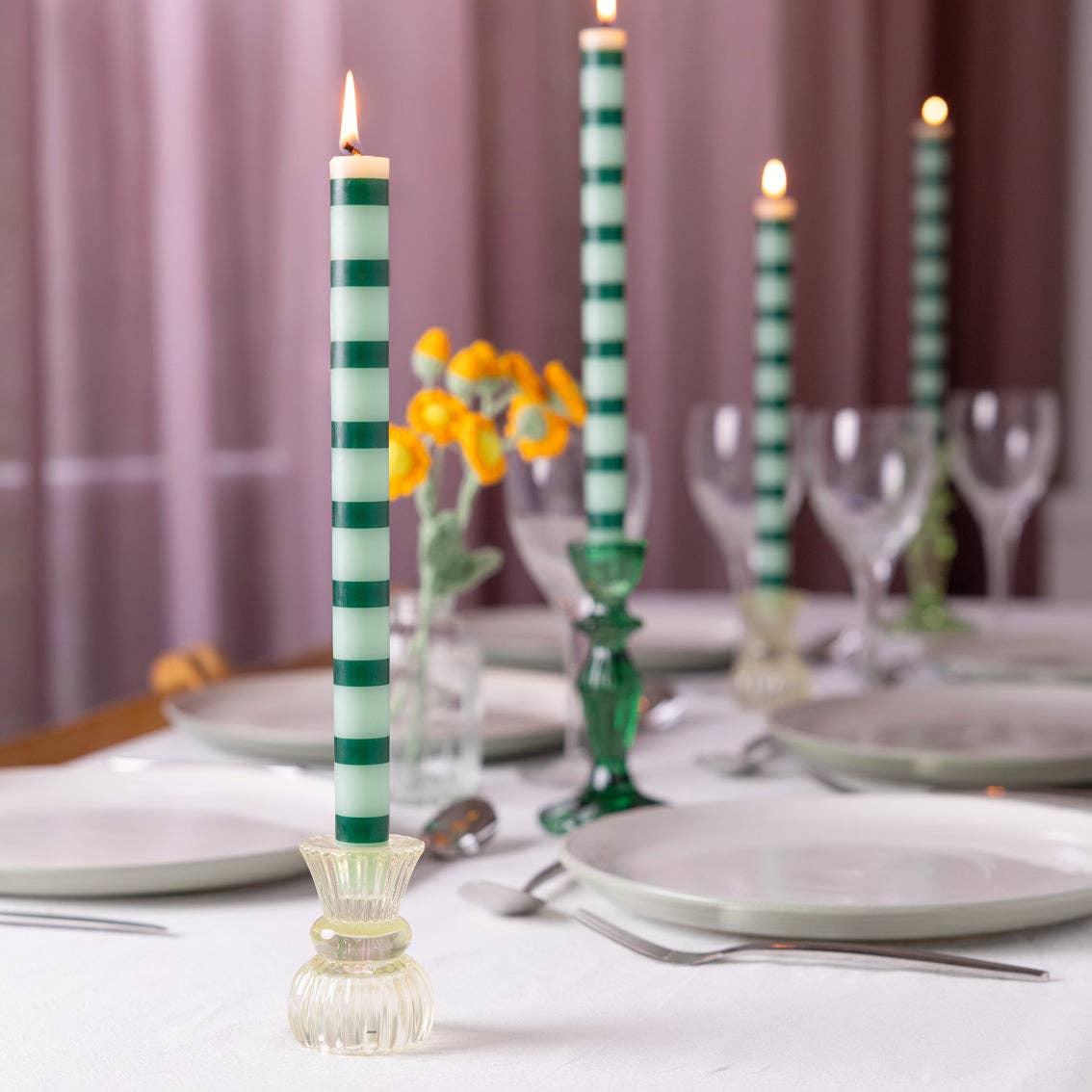 Green and white striped dinner candle with lit flame on clear holder base.