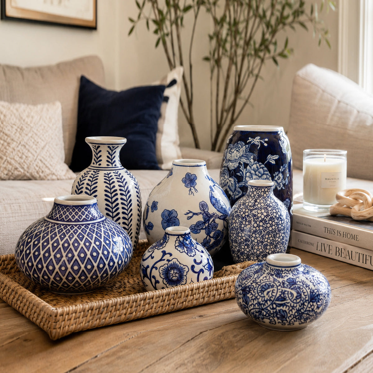 Blue and white ceramic vase set arranged on a woven tray beside decor items