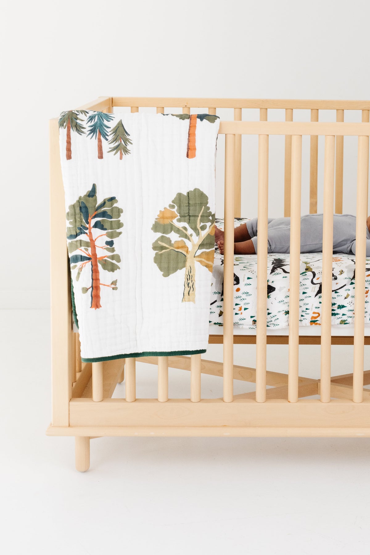 Forest trees quilt draped over crib rail, colorful tree print on white