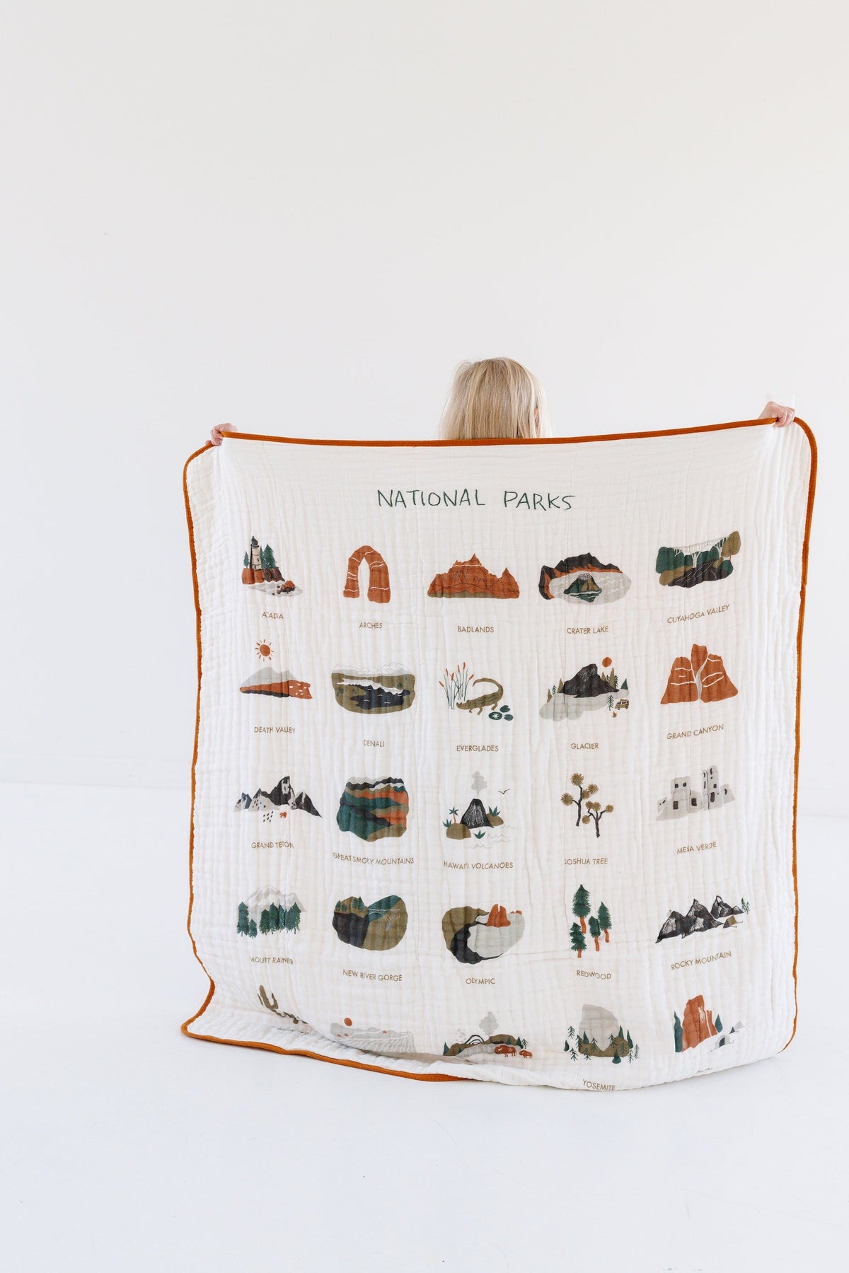 White muslin baby blanket with orange edge trim and national parks map-style prints