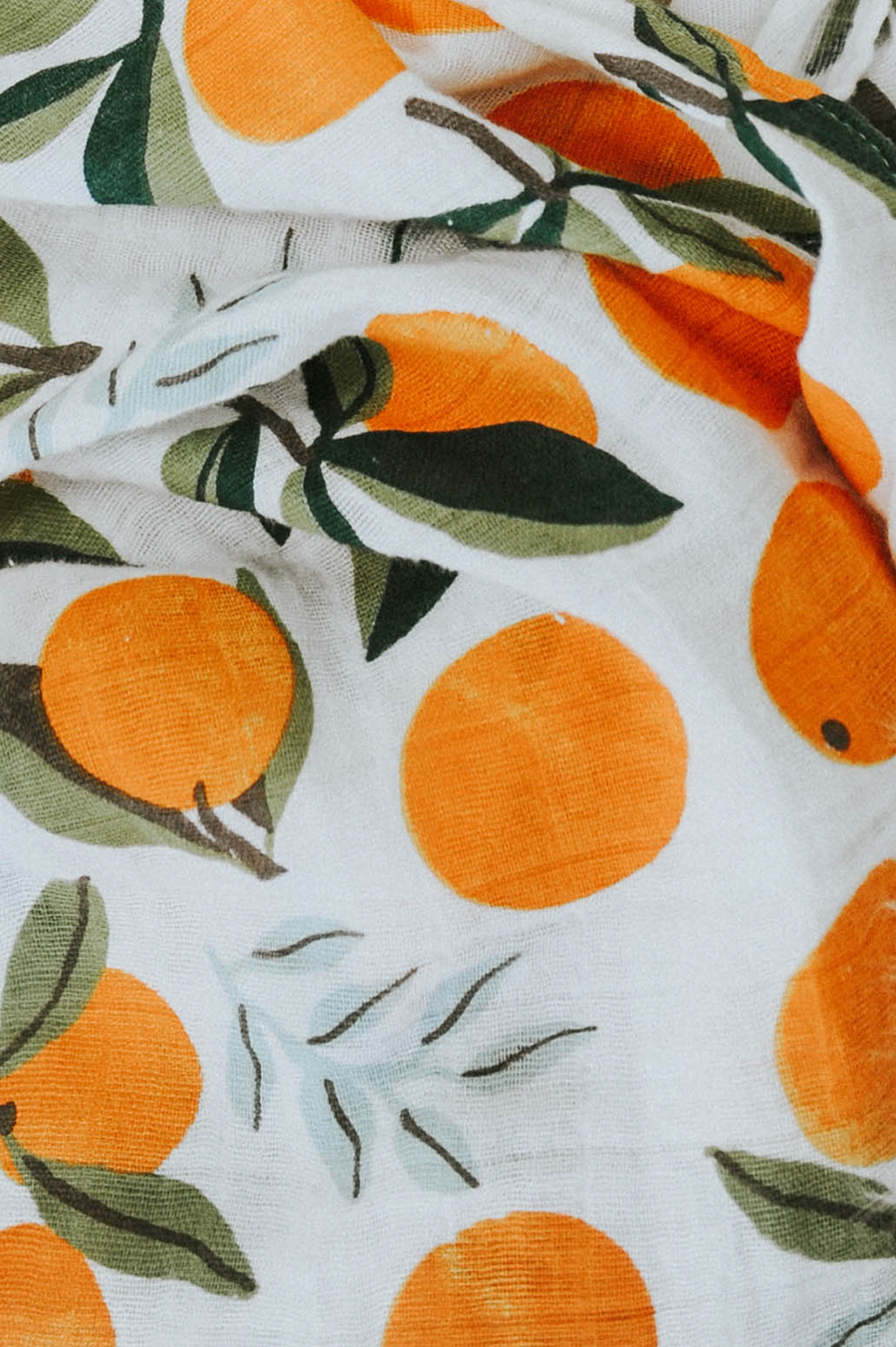 Swaddle fabric close-up: white base with orange fruit and green leaf print.