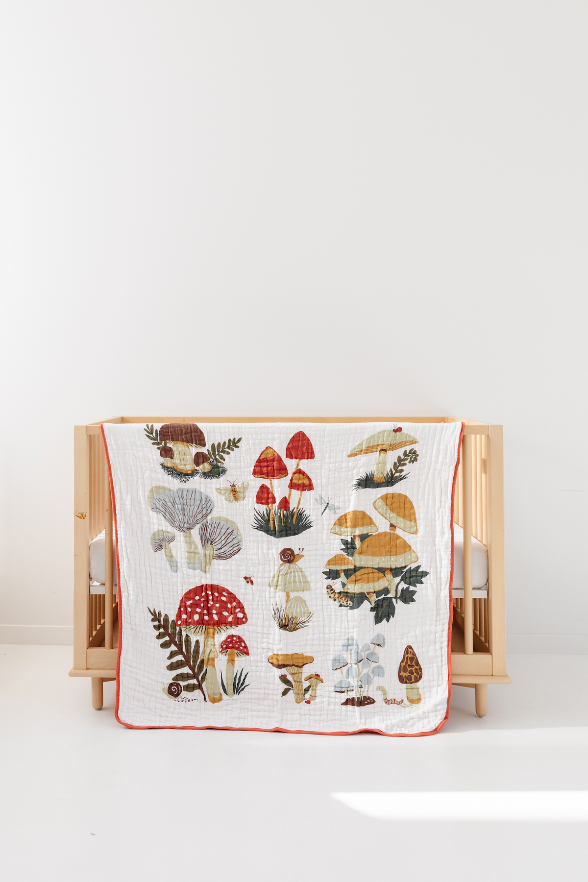 Cotton quilt featuring colorful mushroom illustration pattern with red edge, on crib
