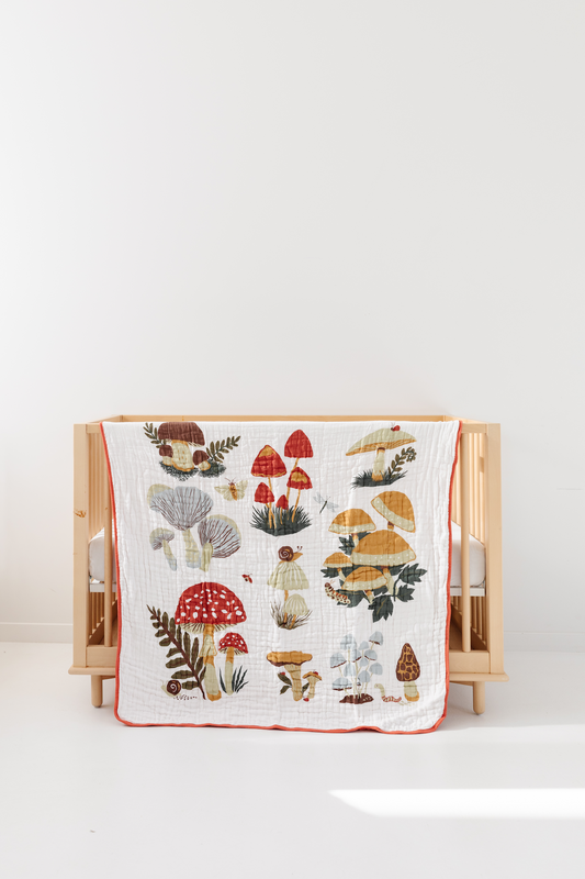 Cotton quilt featuring colorful mushroom illustration pattern with red edge, on crib