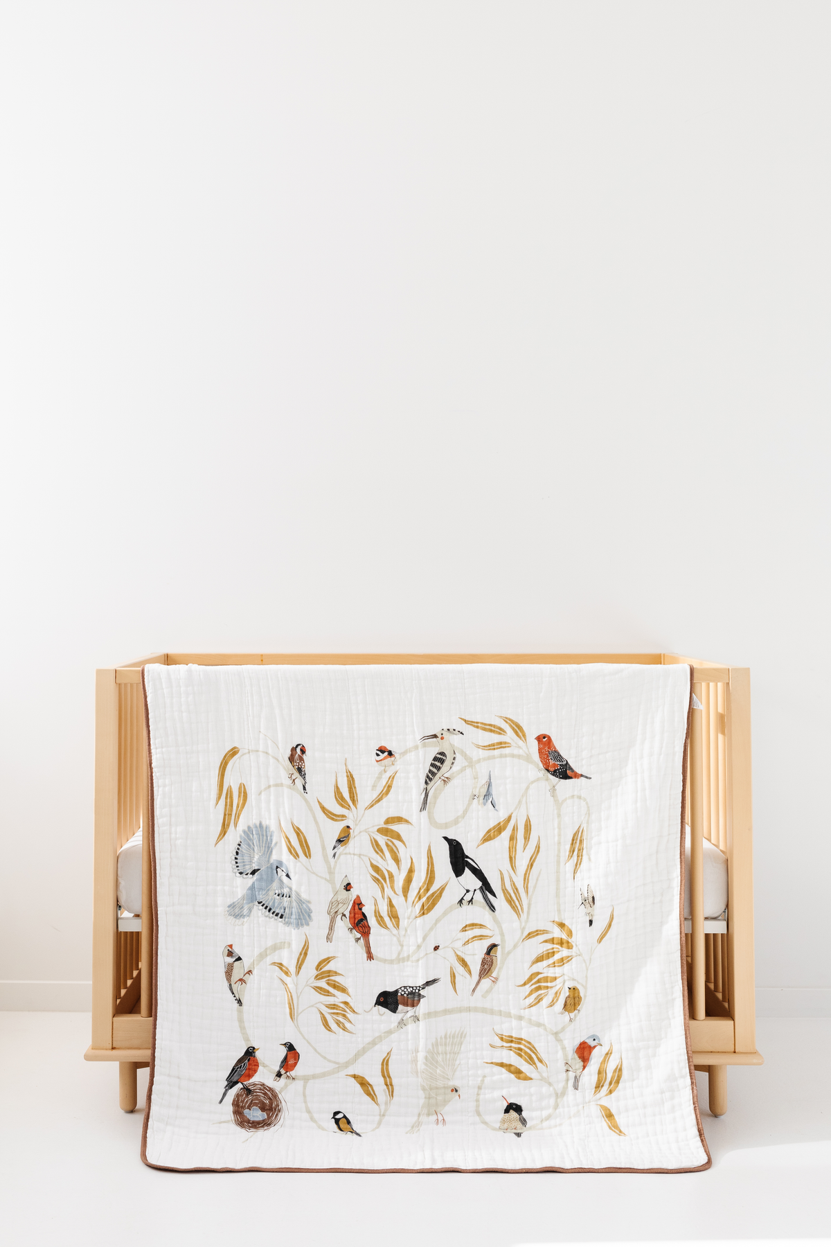 White bird-print quilt with colorful birds and leaves, neatly folded with tan border