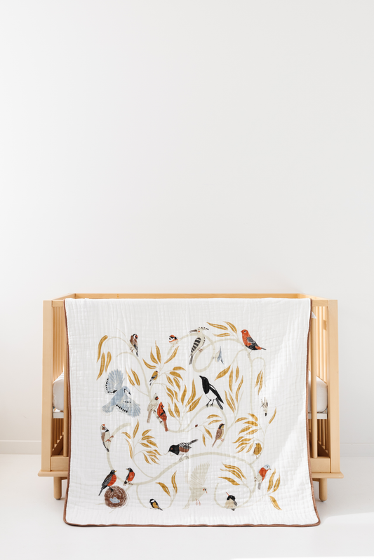 White bird-print quilt with colorful birds and leaves, neatly folded with tan border