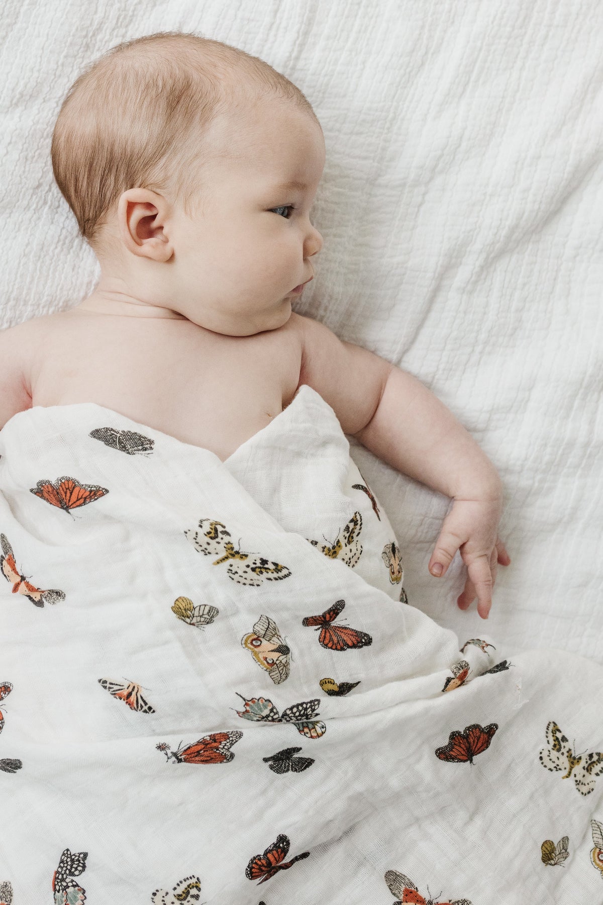 White muslin baby swaddle with butterfly print, baby lying on a soft surface