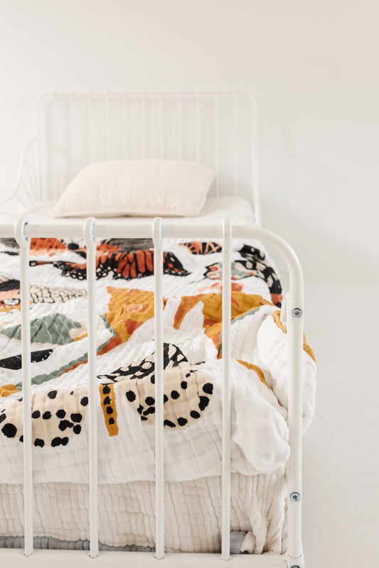 White butterfly throw blanket draped on bed, mustard border on quilted fabric
