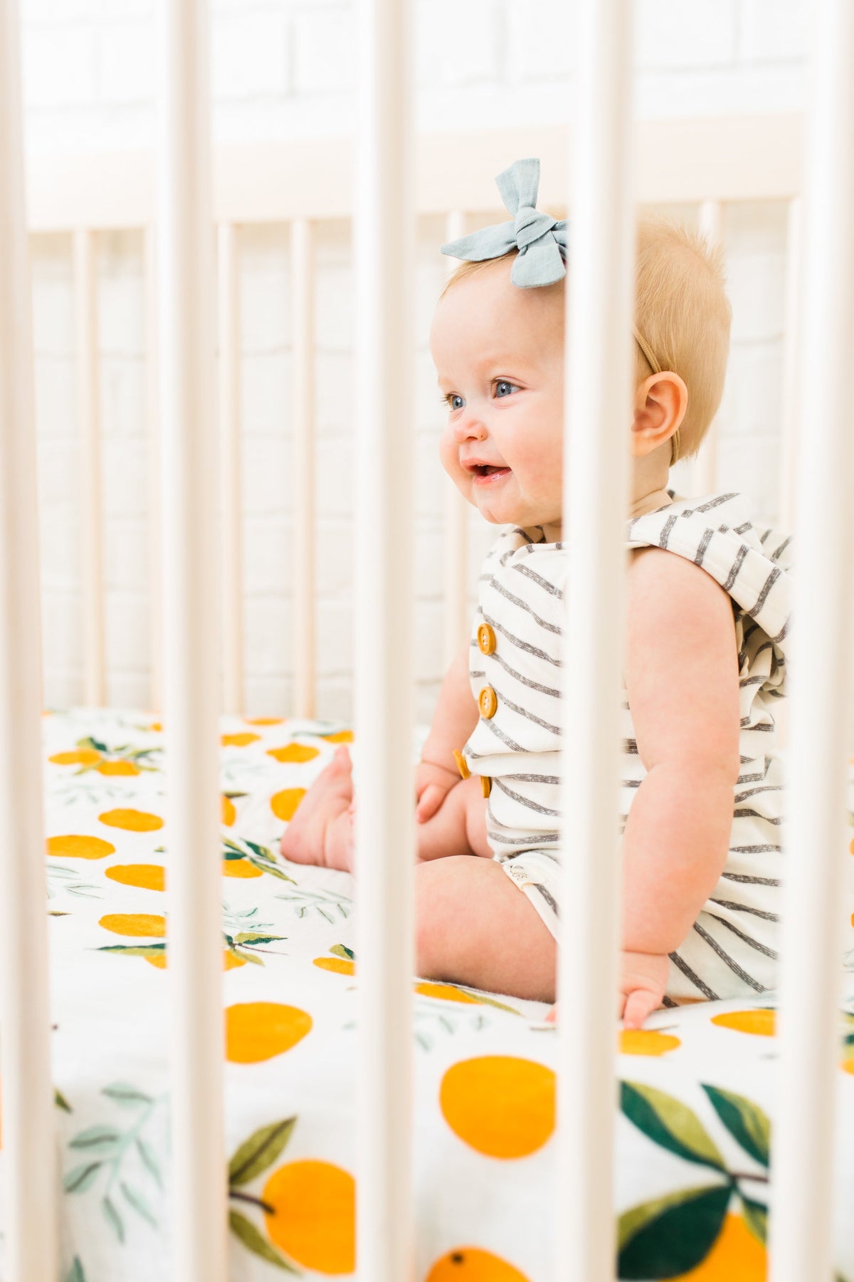 Crib sheet with orange citrus and green leaf print, visible through crib rails