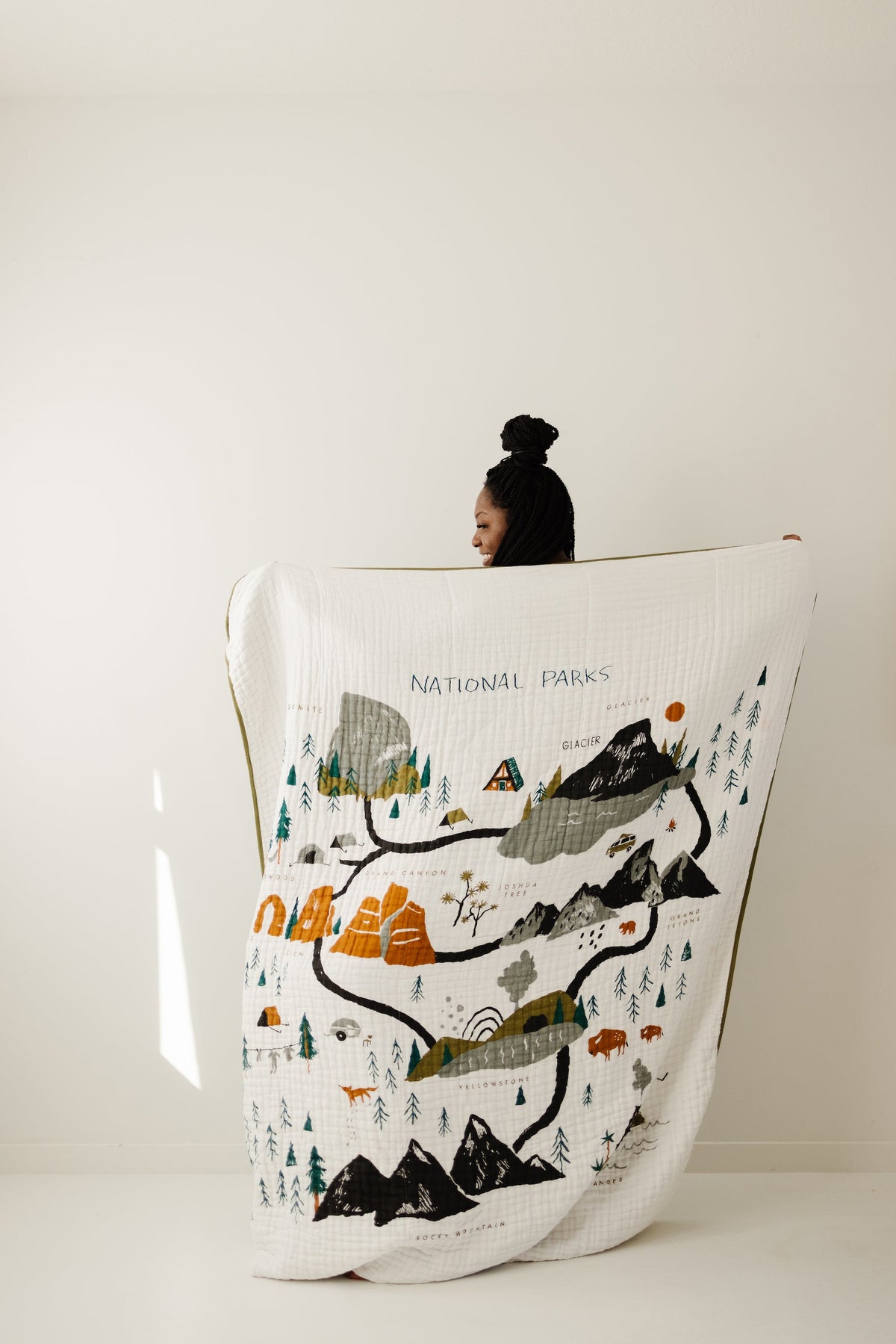 White quilted throw blanket with national park scene: mountains, trees, animals, lettering.