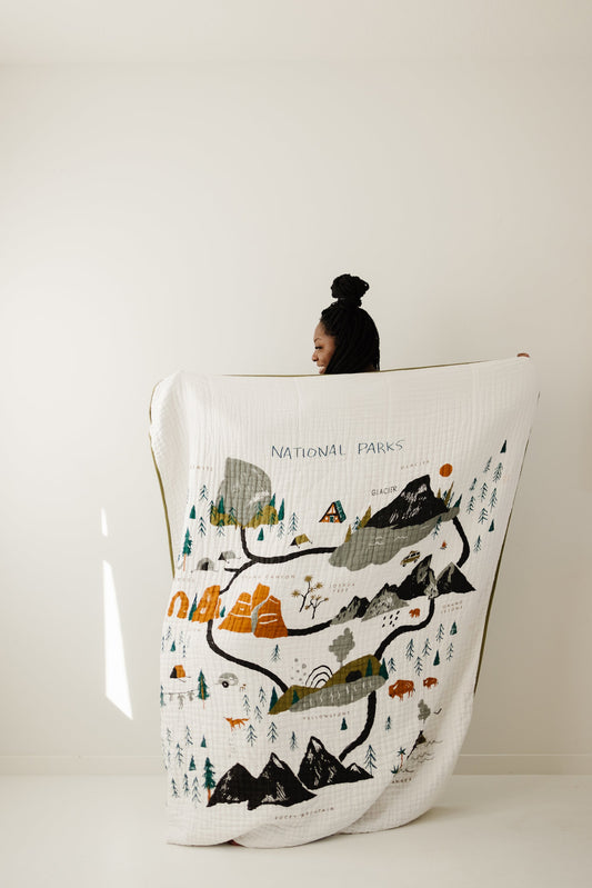 White quilted throw blanket with national park scene: mountains, trees, animals, lettering.