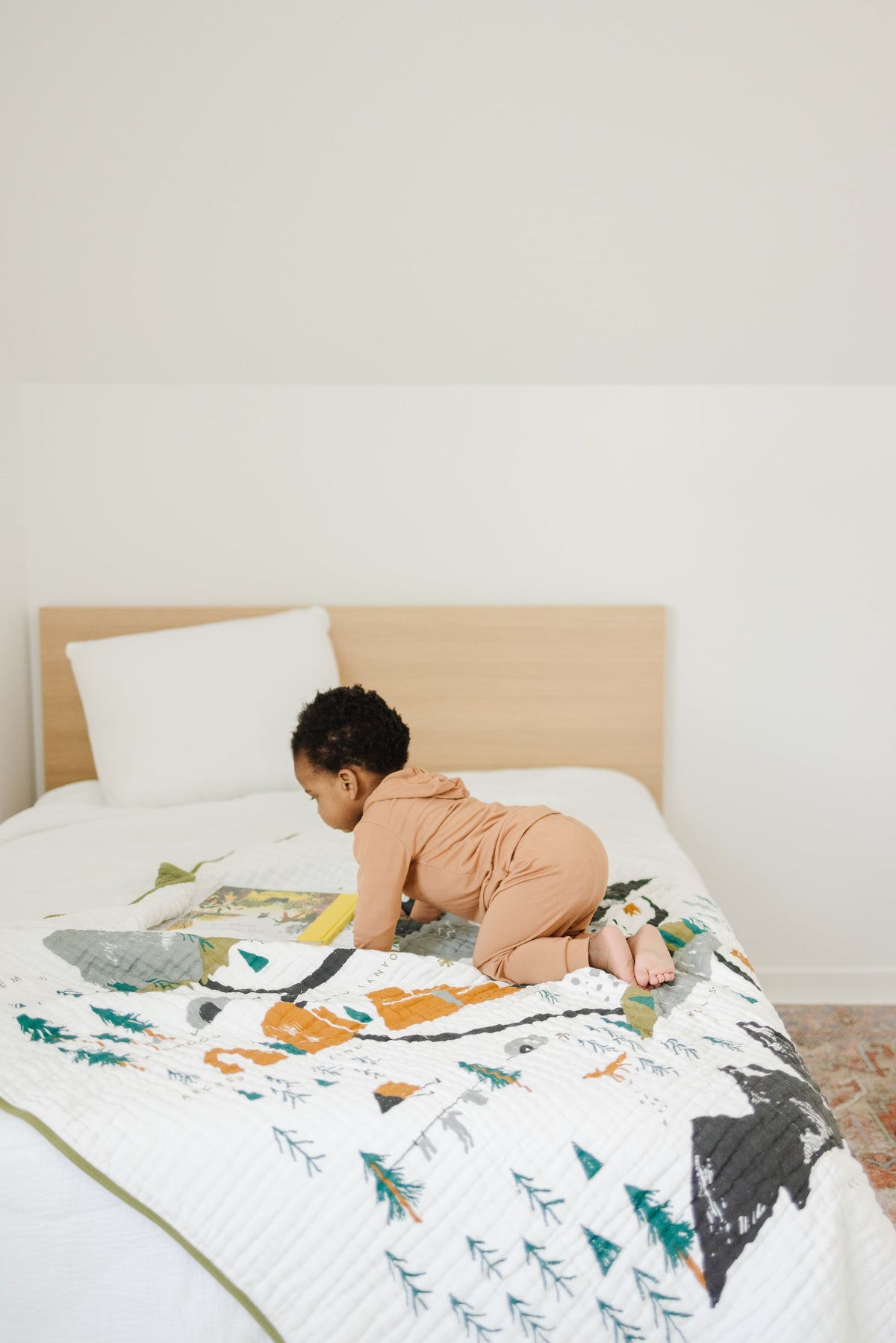 White quilted national park print throw blanket on a bed with mountains, trees, and animals.