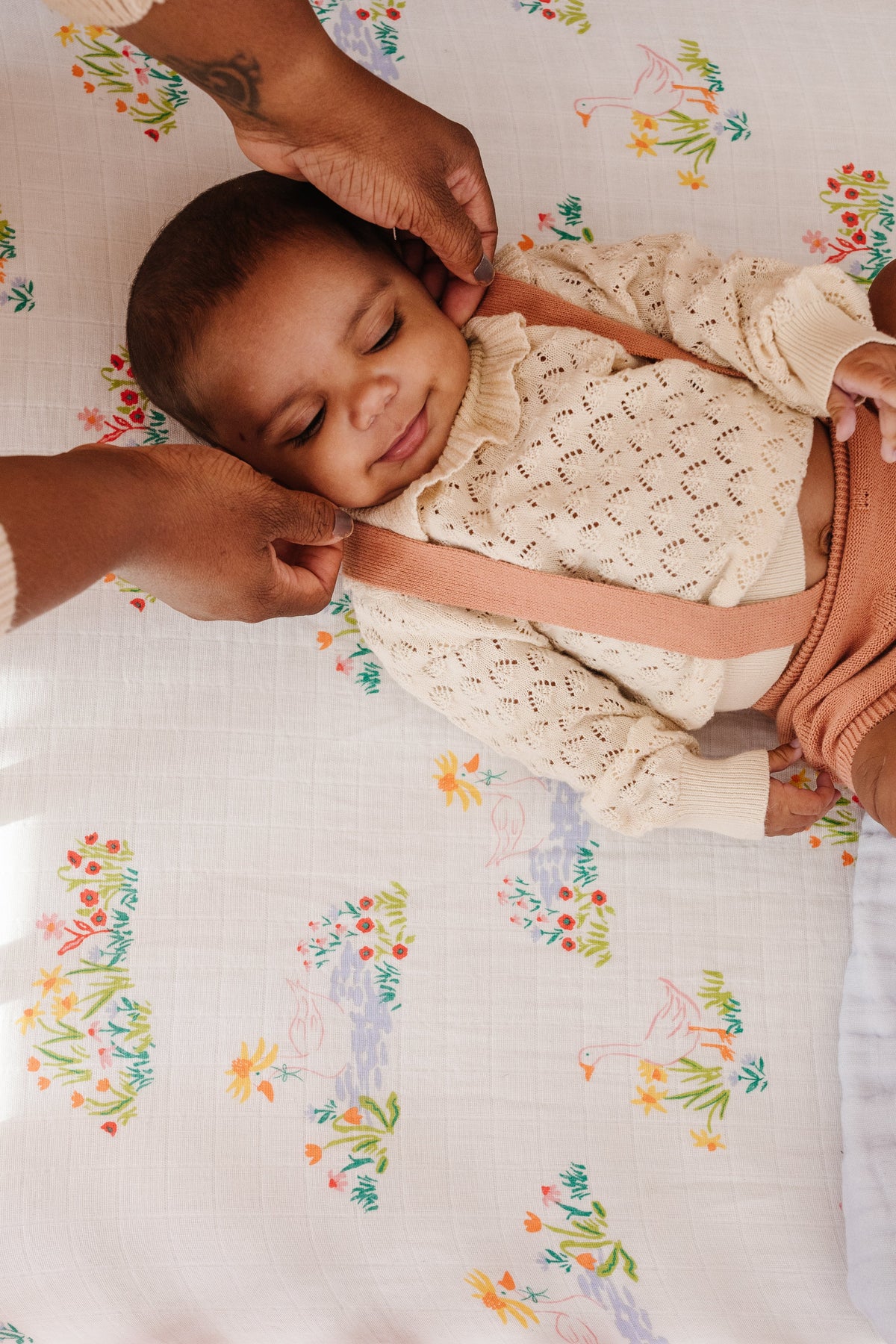 Newborn resting on patterned crib sheet with pastel geese and flowers.