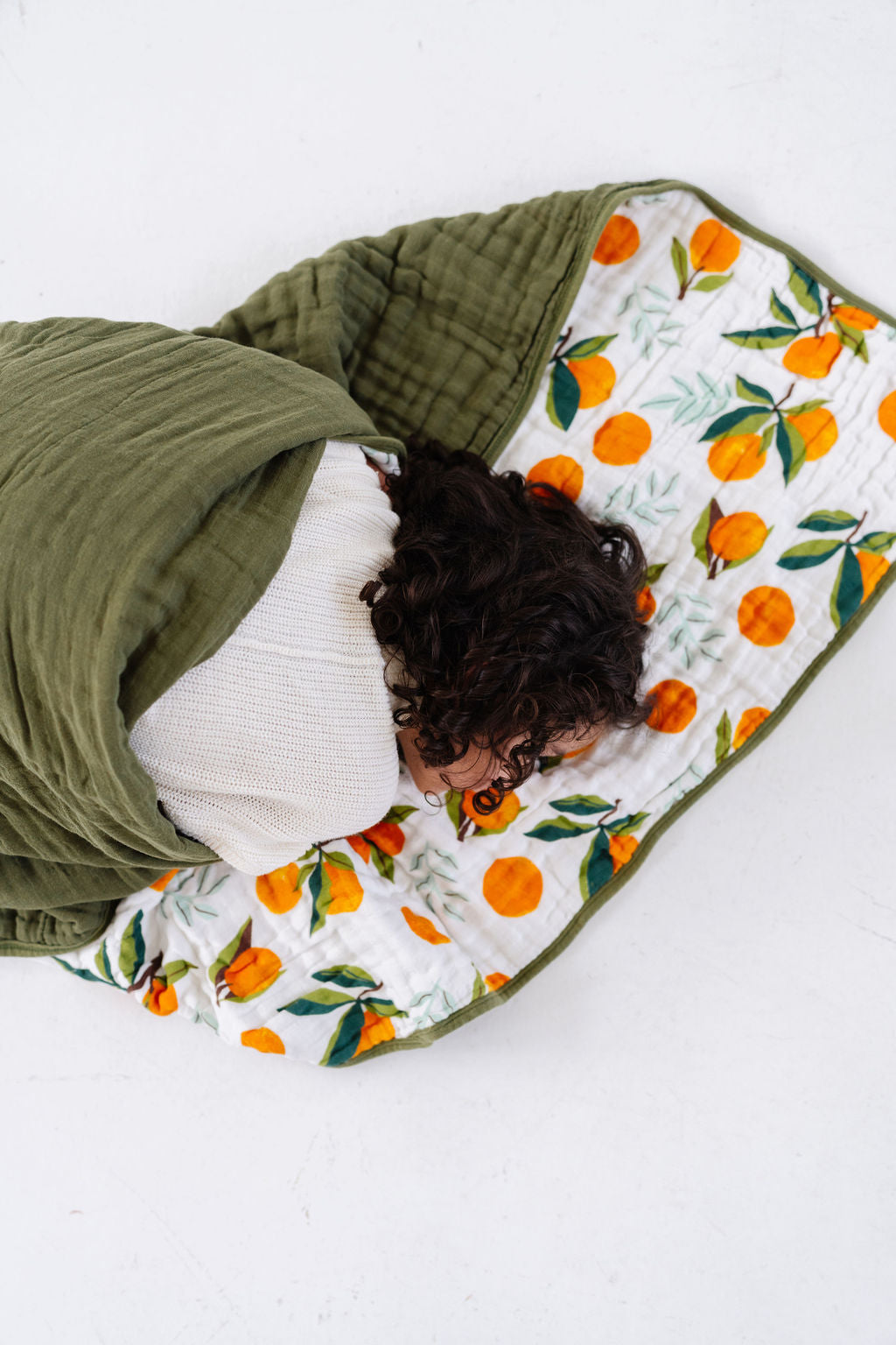 Quilted throw blanket with orange clementine and green leaf print, laid on bed