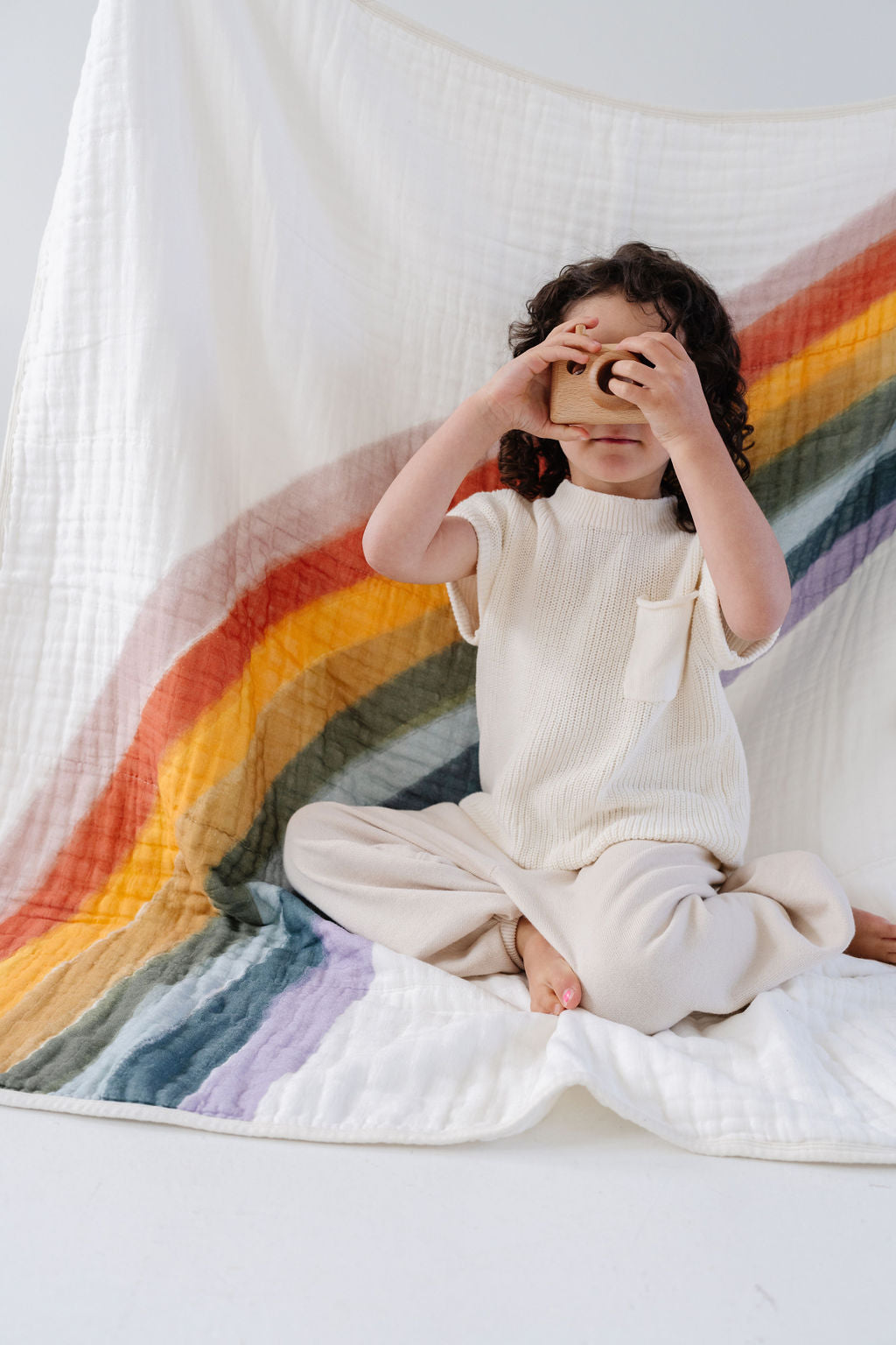 Rainbow arc quilt with white backing, spread beneath a child