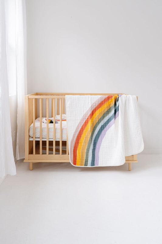 Rainbow striped quilt draped over white crib blanket, colorful arch design