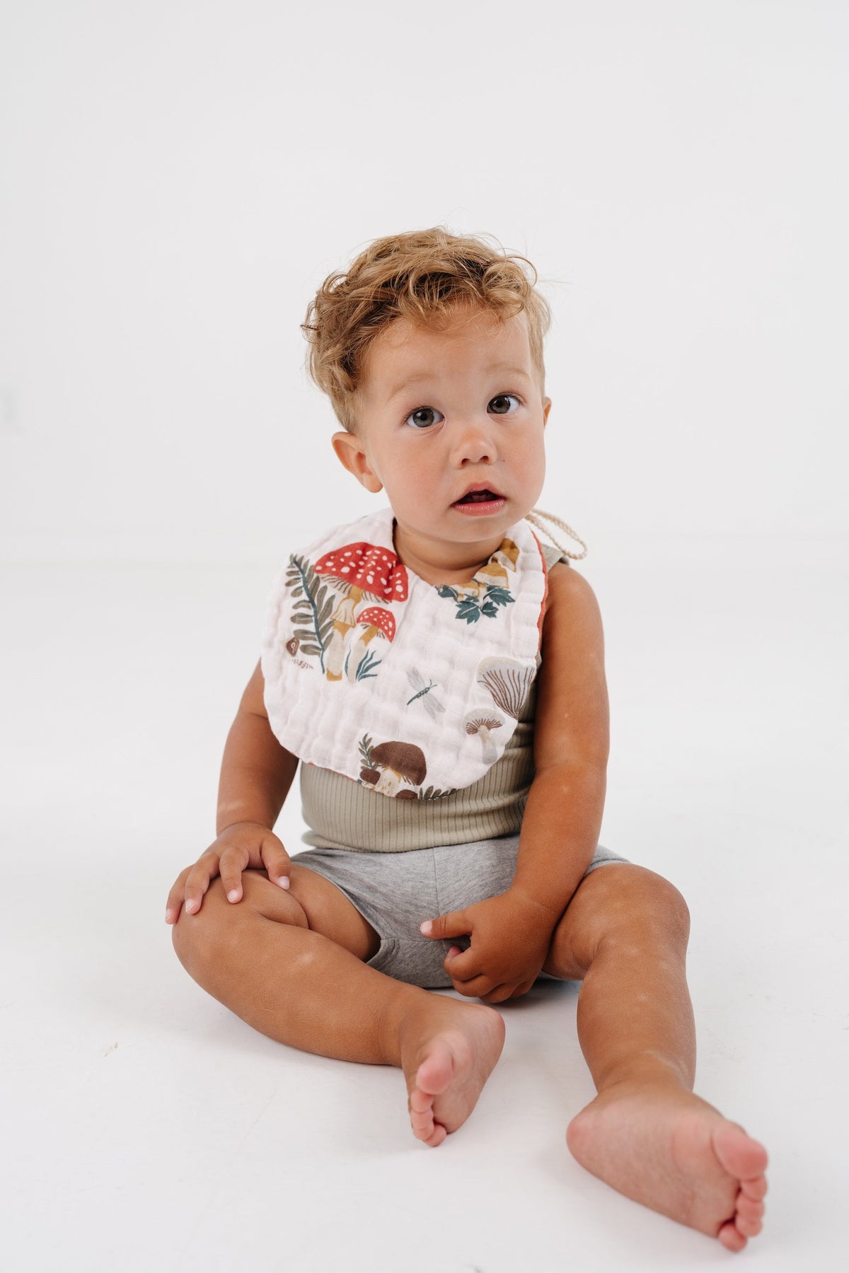 Sleeveless mushroom bib with beige edge, baby seated with legs out