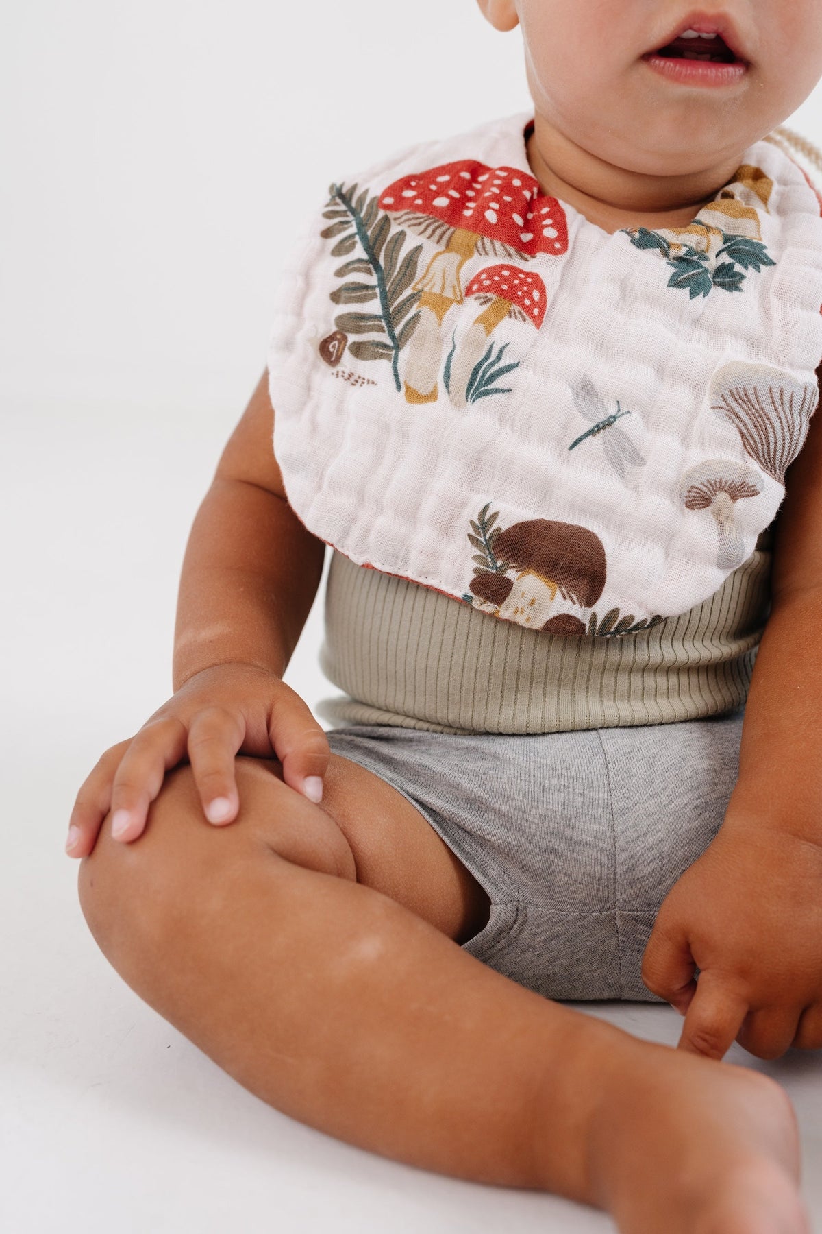 White bib with mushroom and forest animal print, worn by baby