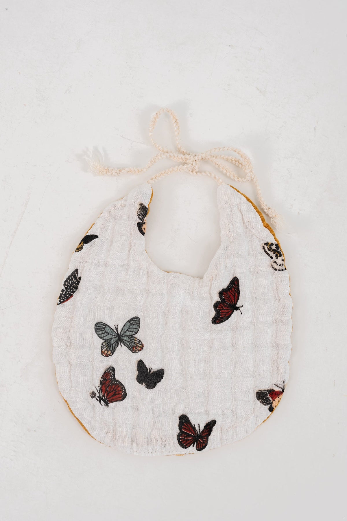 White muslin baby bib with multicolor butterfly pattern and scalloped neck tie