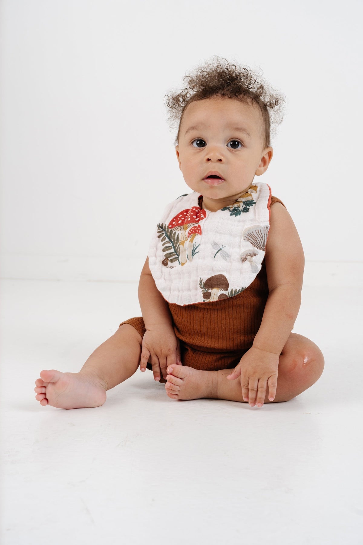 Baby wearing mushroom and forest animal print bib, beige trim
