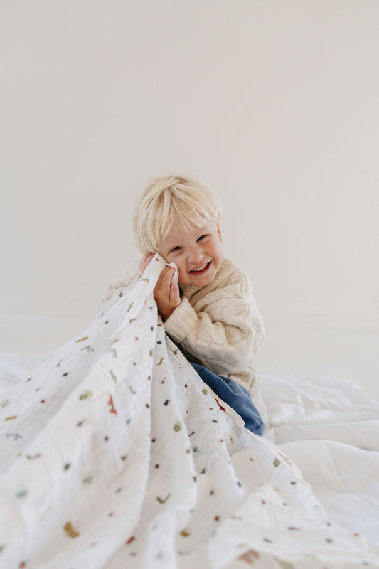 White baby swaddle blanket with tiny animal print, covering toddler on bed