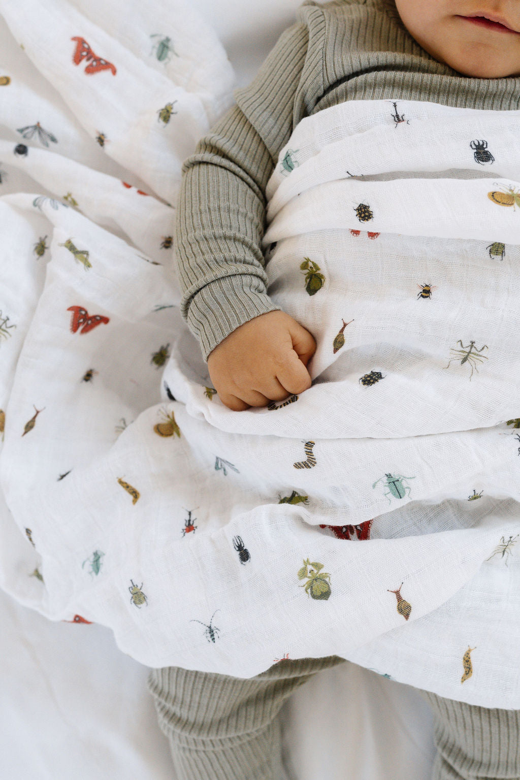 White baby swaddle blanket with small animal print, wrapped around infant
