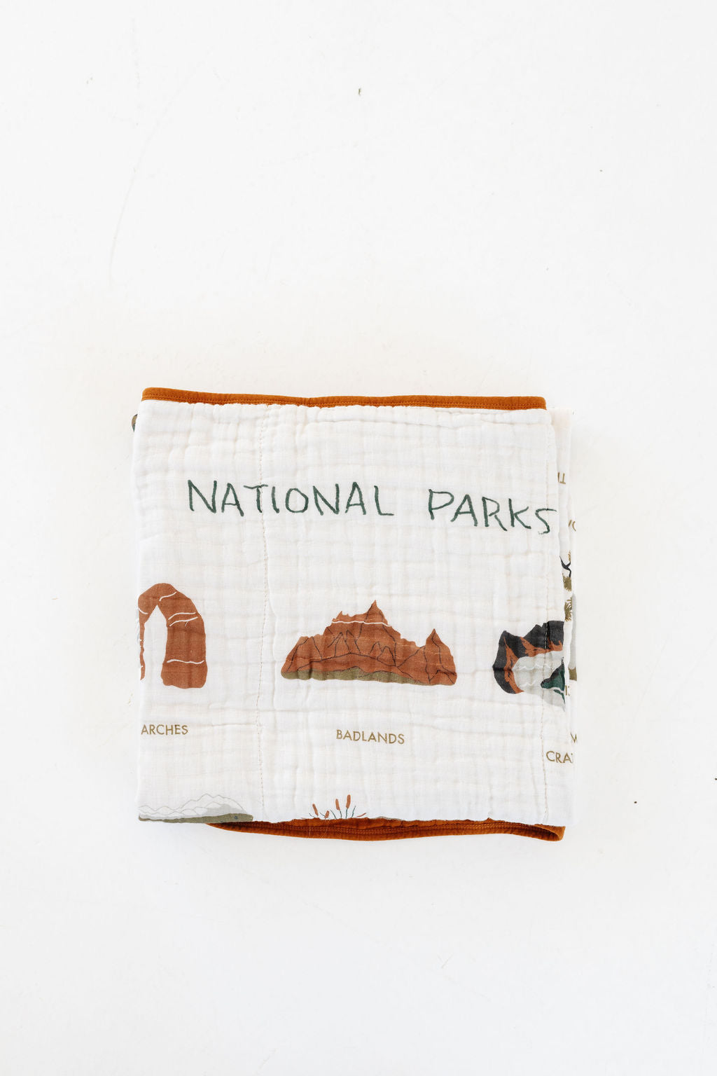 Folded white muslin blanket with orange trim, illustrated park icons, and text