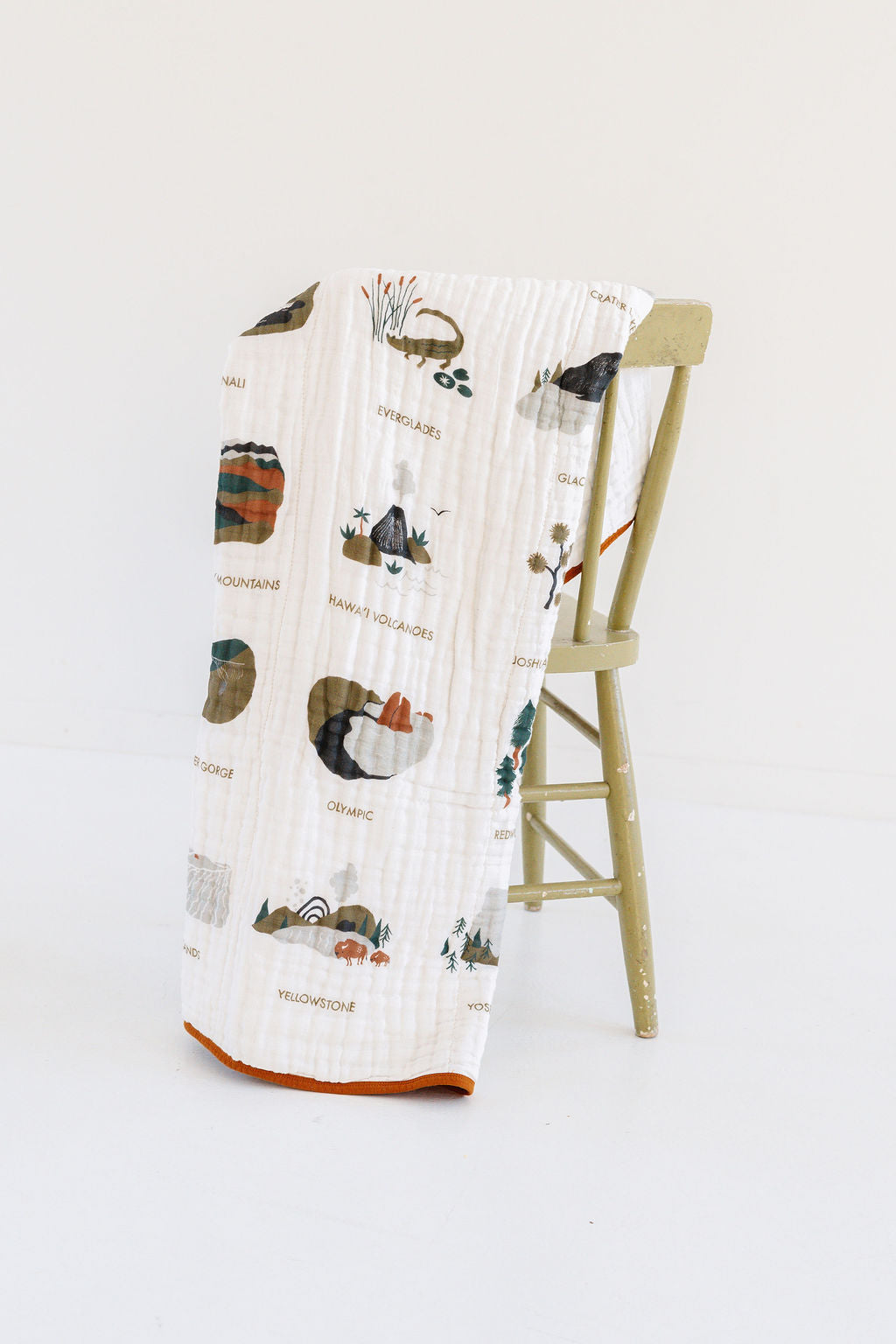 White muslin blanket draped over chair with orange trim and illustrated park scenes