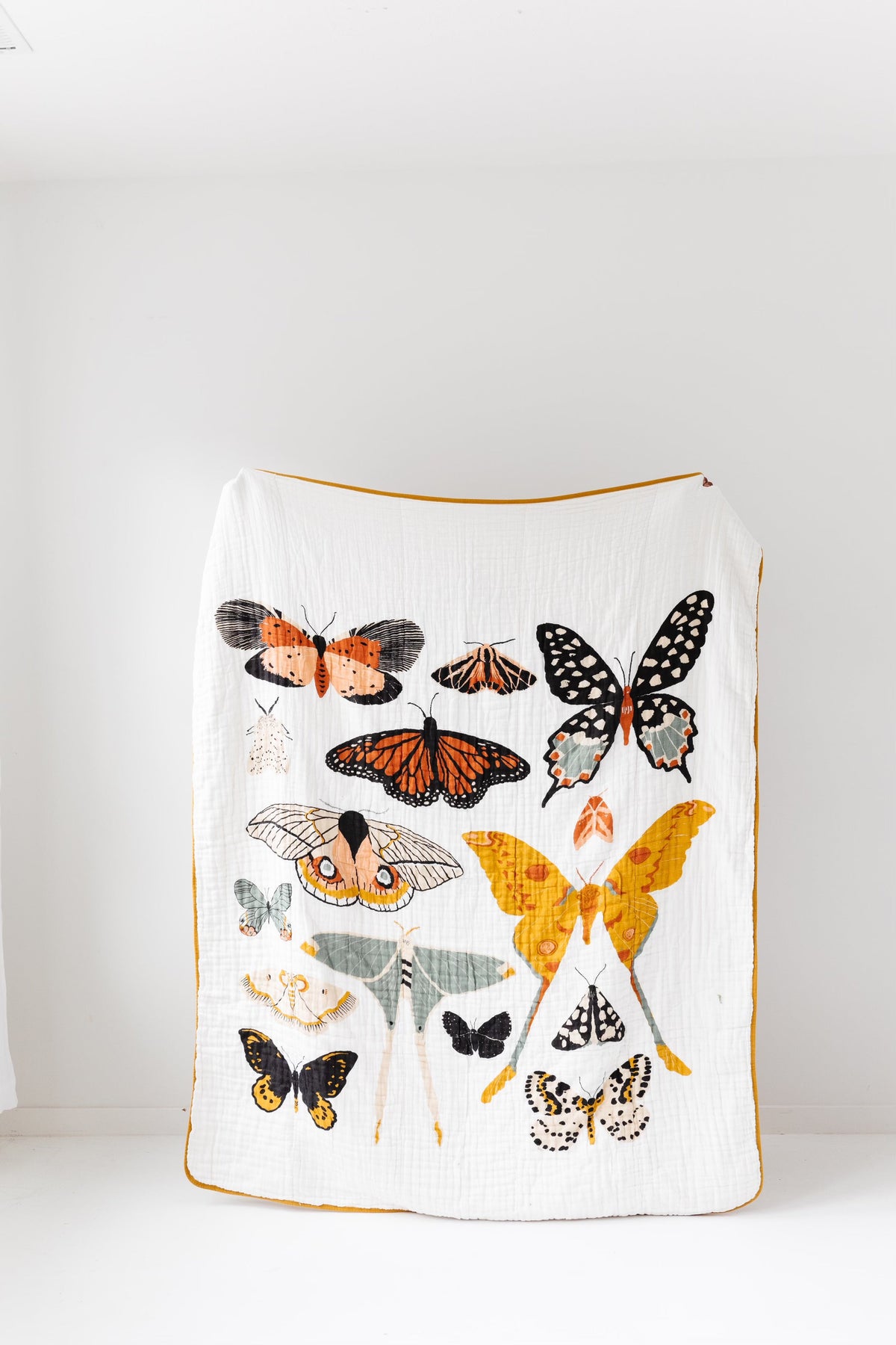 White throw blanket with multicolor butterfly print and mustard-yellow edging, quilted texture