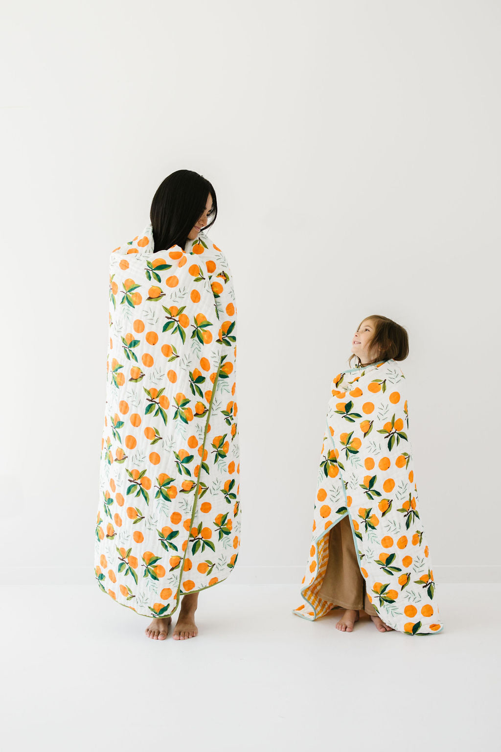 Two views of white throw blanket with orange clementine and green leaf print