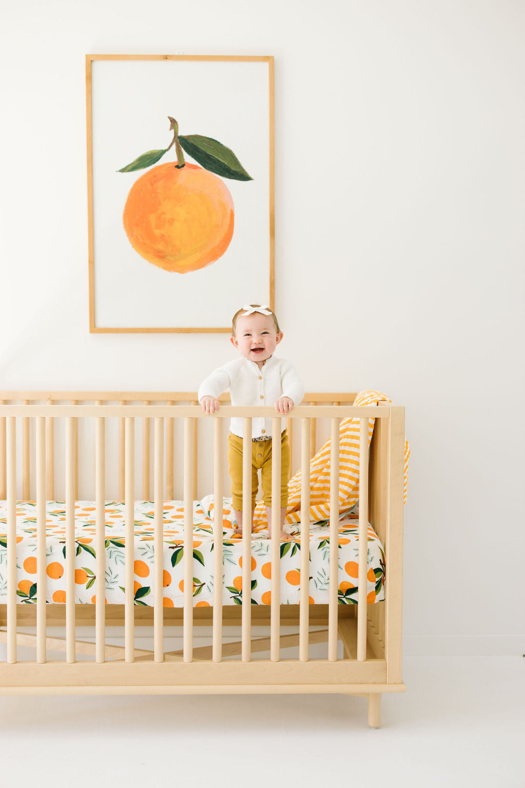 Crib sheet on a light wood crib, featuring orange citrus and green leaf print