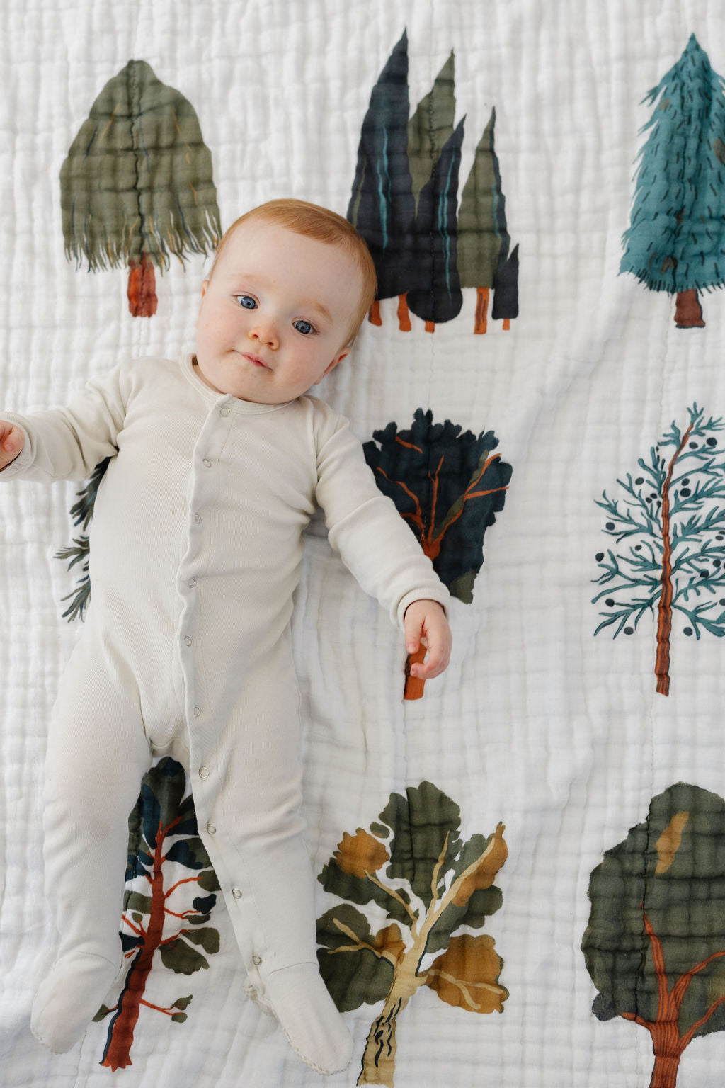 Kids forest trees quilt with colorful woodland prints, baby lying on white fabric
