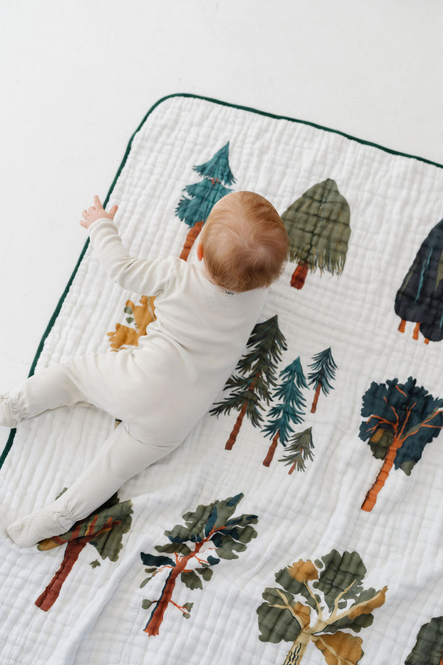 Forest trees quilt close-up with green-trim edge and woodland prints; baby crawling
