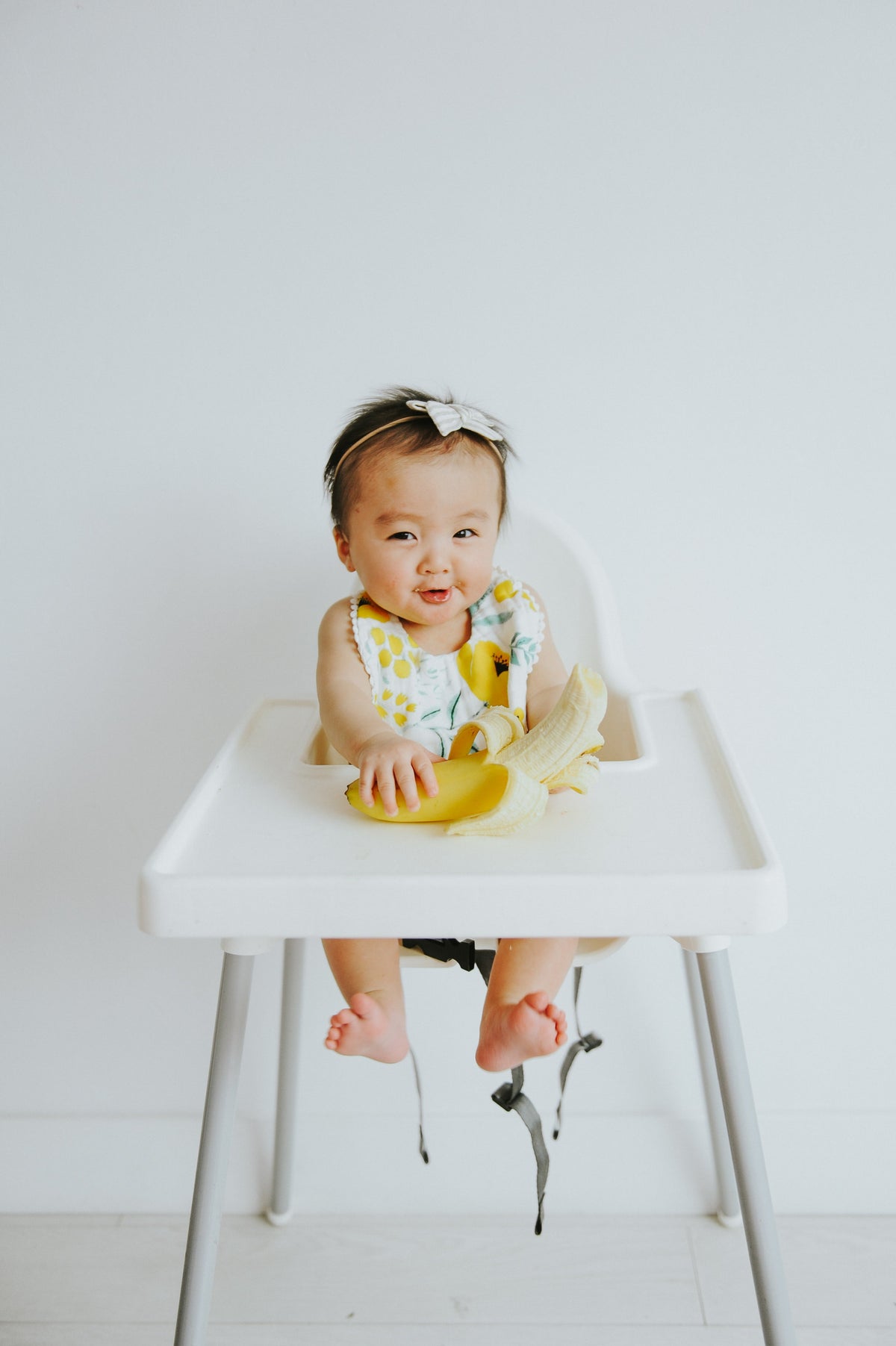 Baby bib with yellow and white floral print and ruffled trim, worn with long-sleeve outfit