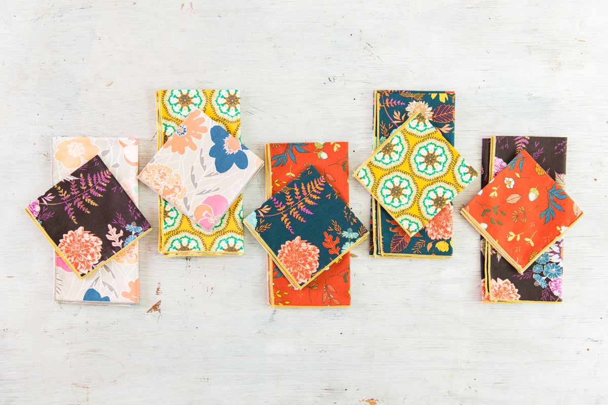 Set of four folded floral cloth napkins with bright orange, teal, and navy designs