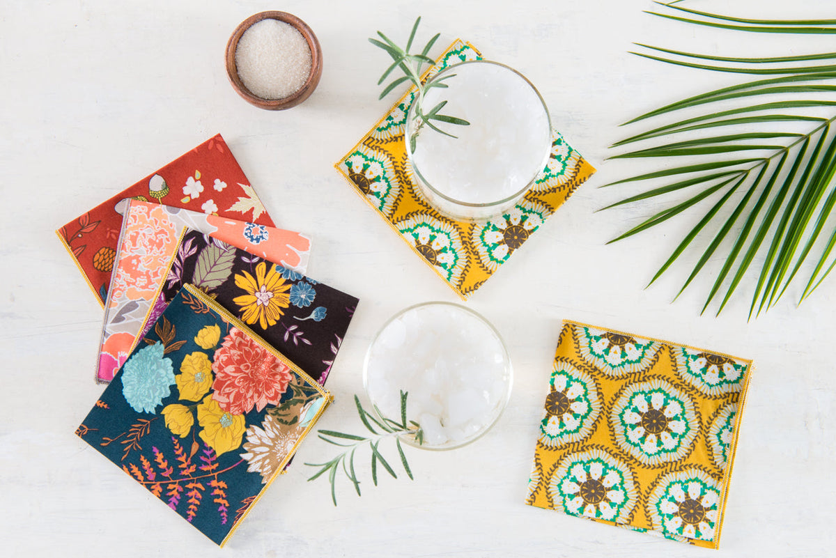 Four floral cloth napkins with gold-trim borders in navy, teal, and coral tones