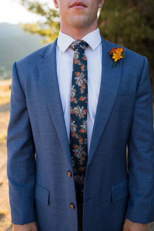 Men's floral necktie with orange and white pattern, worn with blue suit