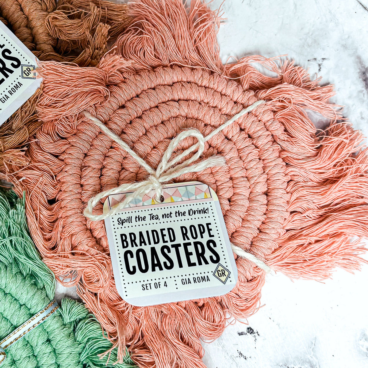 Close-up braided rope tassel coaster with peach tones and a hanging product tag