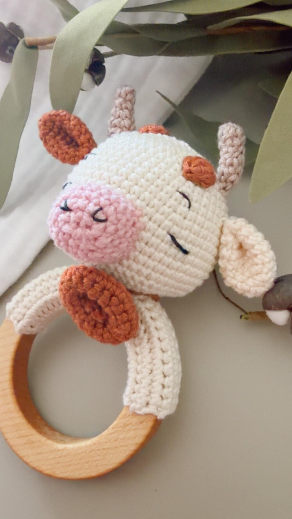 Crochet plush cow rattle with wooden ring and stitched horns, legs, and tail