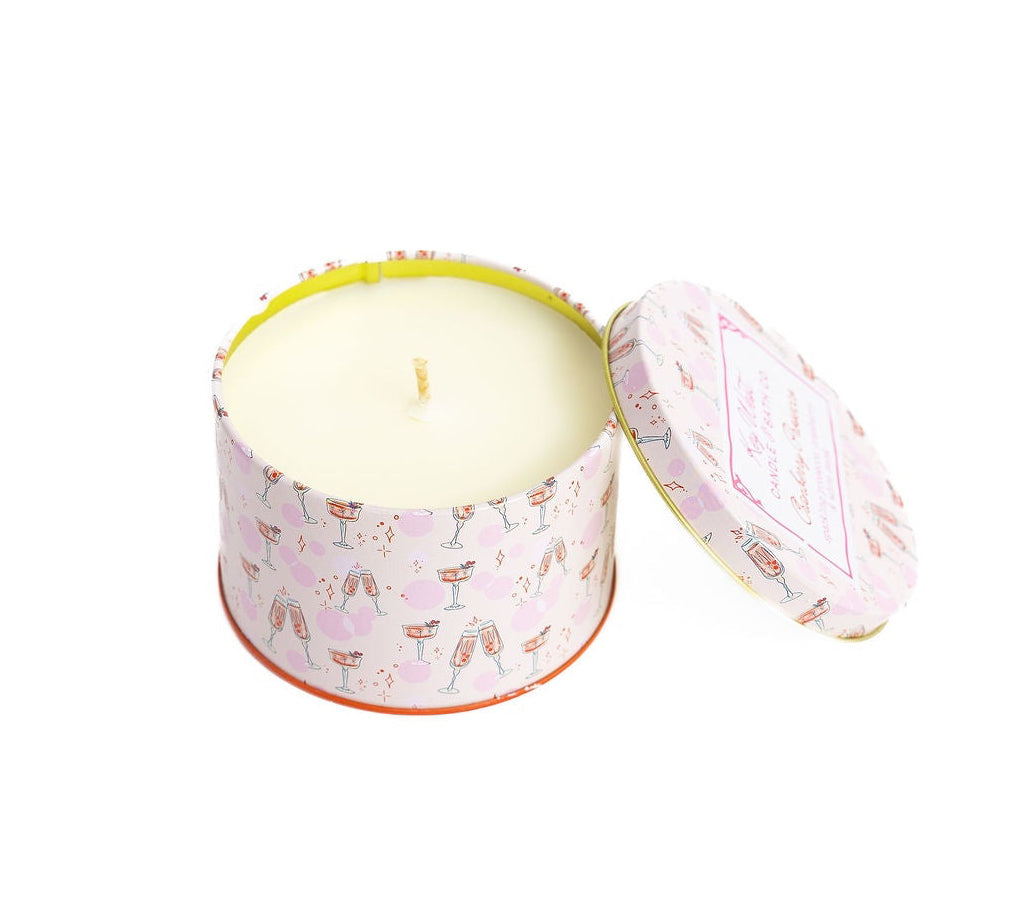 Travel tin candle with open lid showing pale yellow wax and pink drink-print exterior