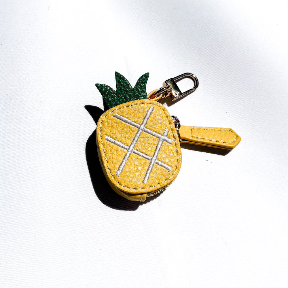 Pineapple-shaped leather keychain charm with green leaf detail and stitched grid.