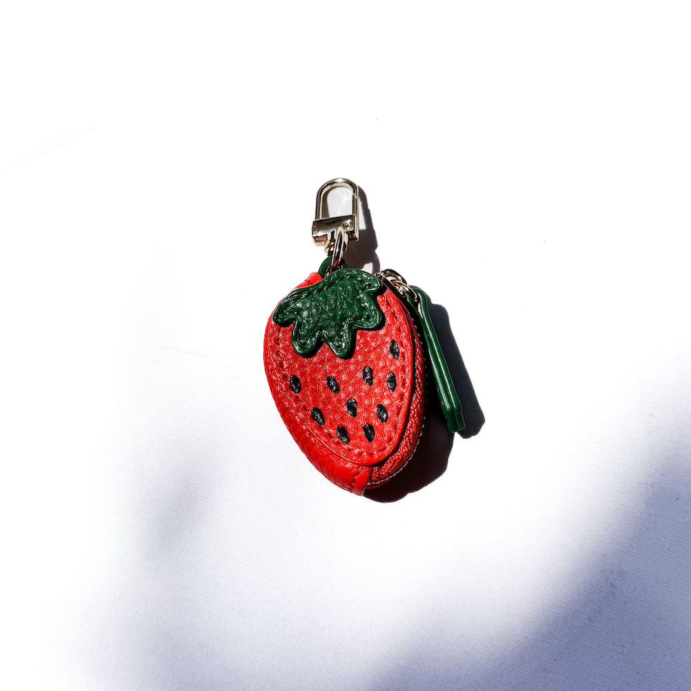 Strawberry-shaped leather keychain charm with green leaves and black seed dots.