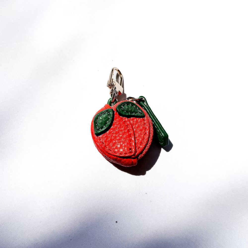 Strawberry-shaped leather keychain charm with green leaves and split red design.
