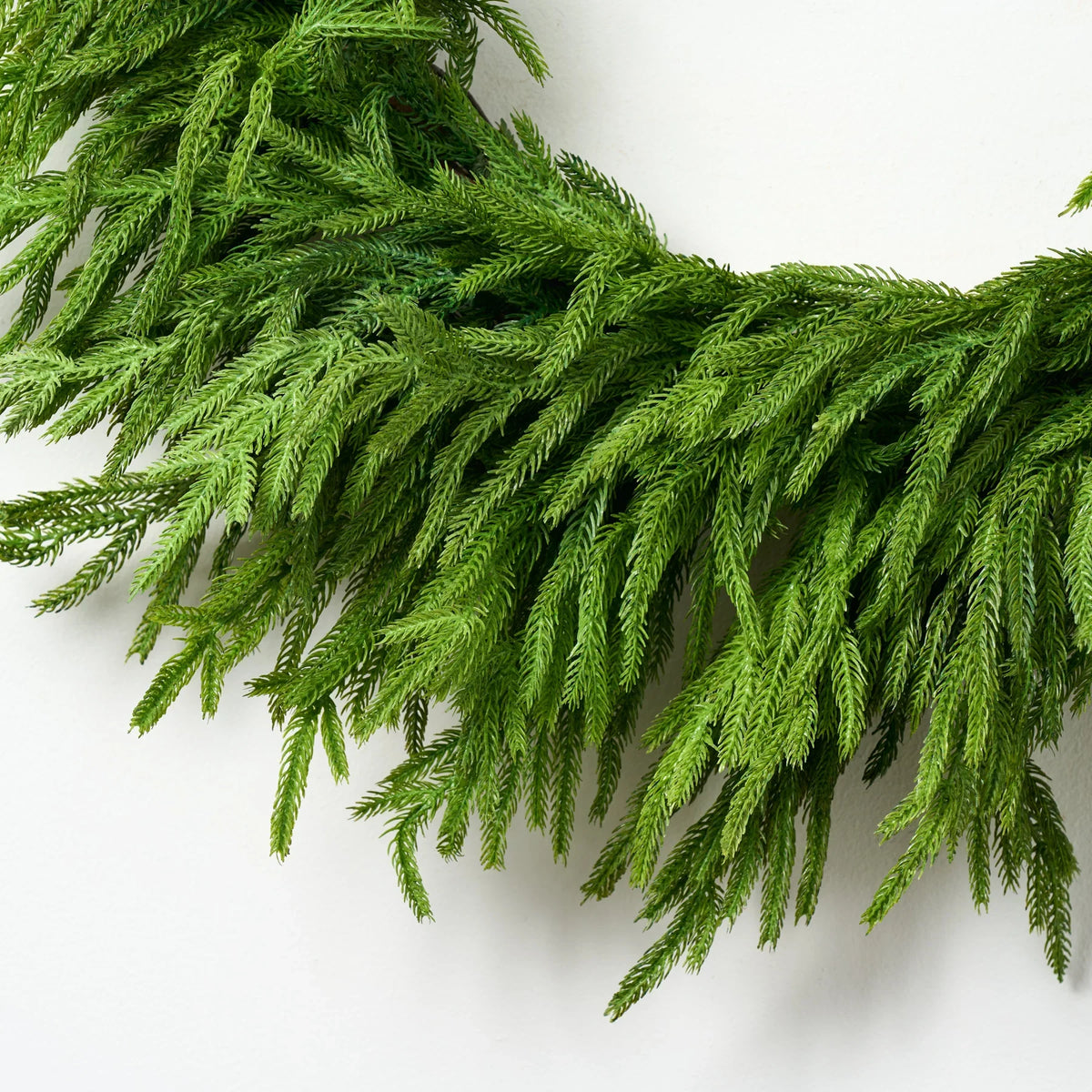 Green faux pine Christmas wreath with textured branch details, partial close-up.