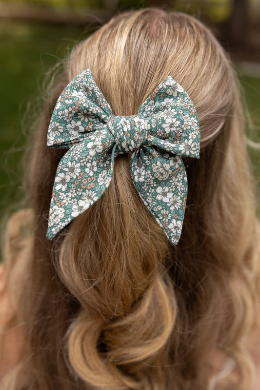 Floral hair bow tied in blonde hair with two looped ends and trailing tails