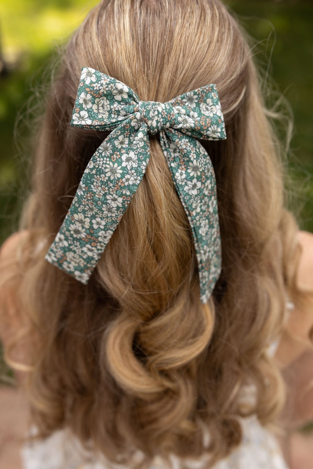 Green floral lady hair bow worn in light brown hair with long ribbon streamers